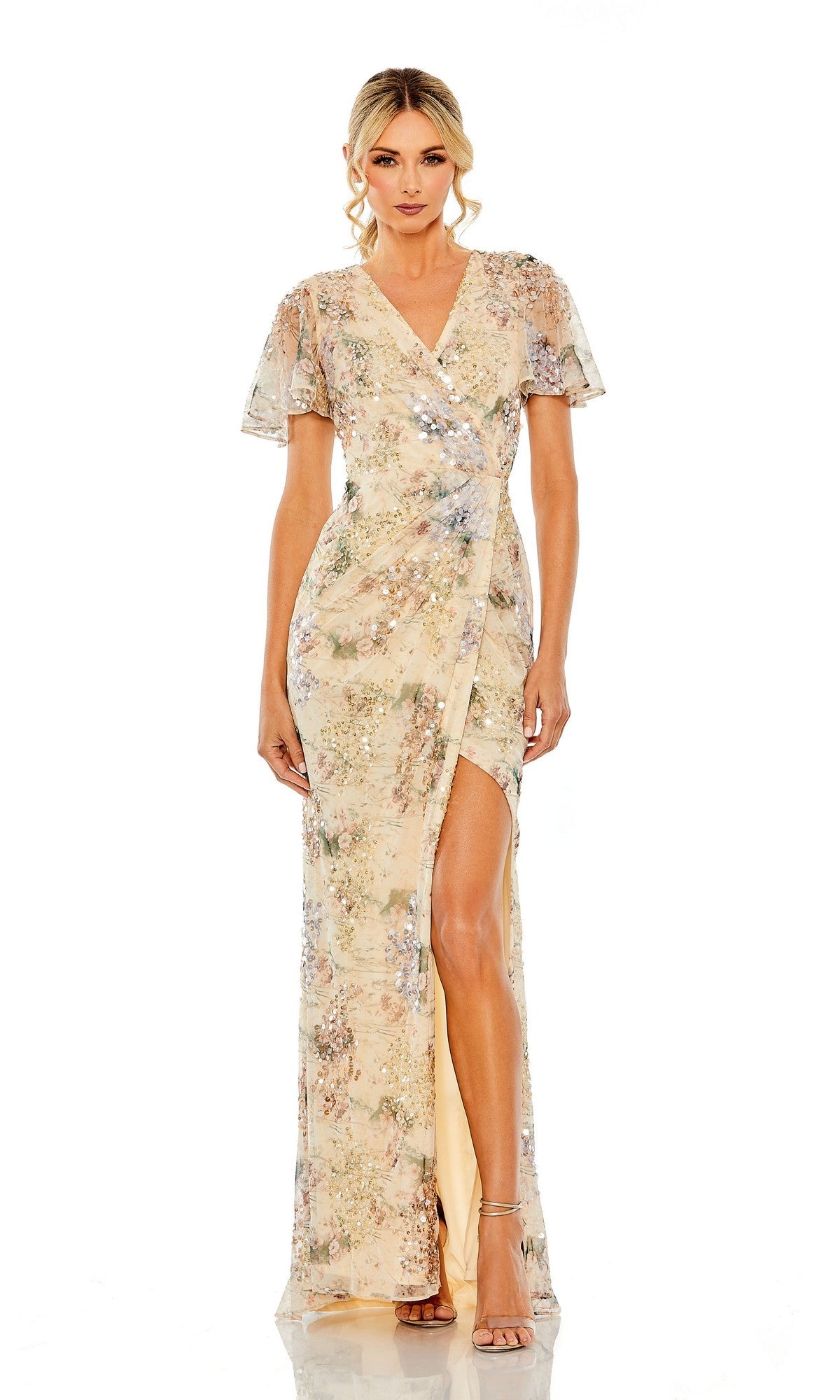 A woman stands against a white background in the Mac Duggal 93749 Short Sleeve Beaded Formal Dress, a light-colored wrap gown with floral sequins, short sleeves, and a high slit—radiating elegant evening style.